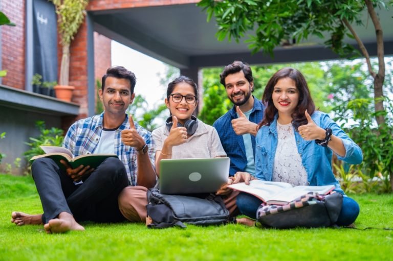 Young,Indian,College,Friends,Sitting,Comfortably,On,A,Green,Lawn